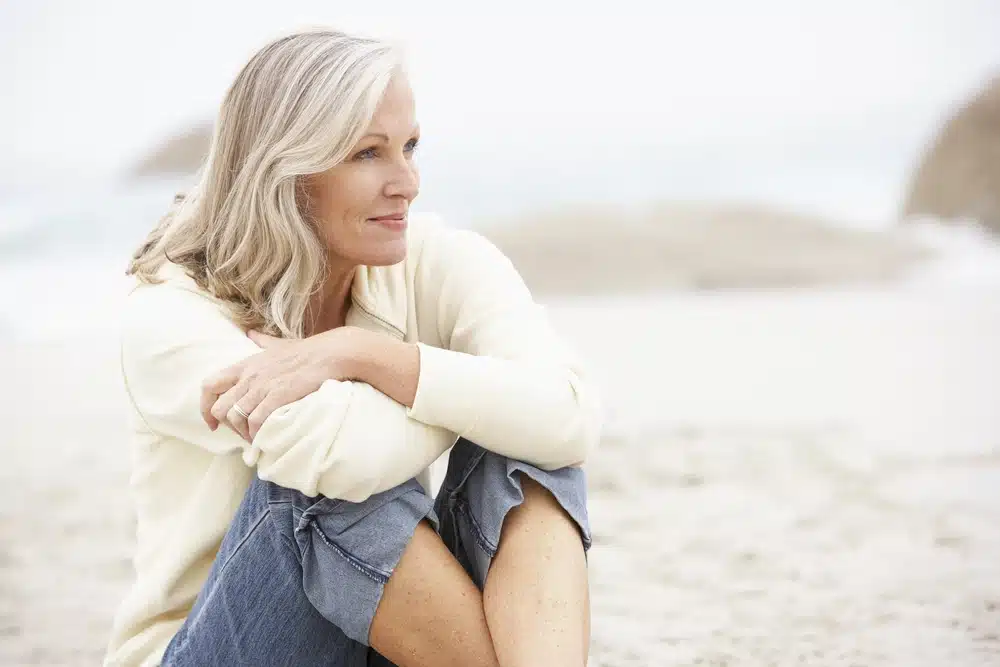 mature woman sitting on the beach staring into the distance