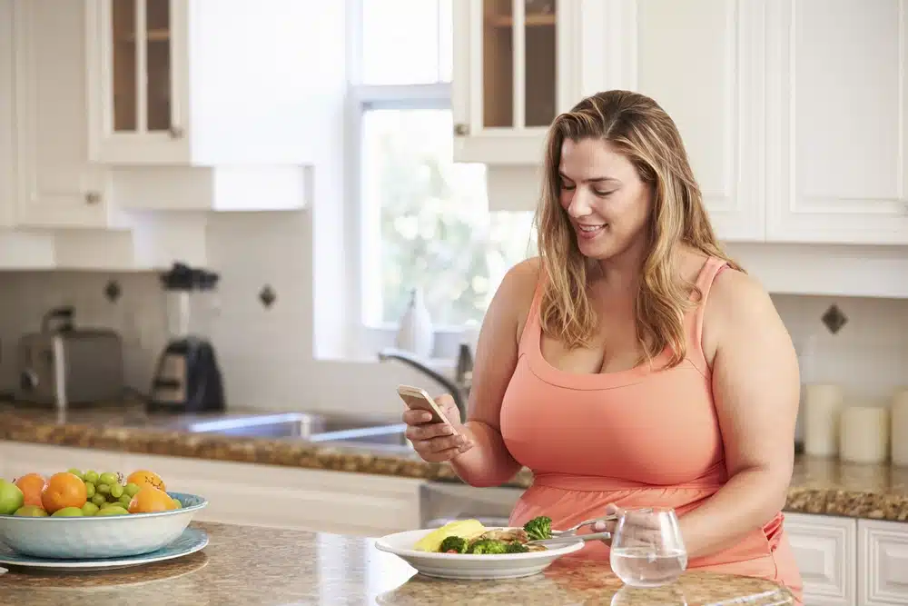 woman eating a healthy meal and looking at phone